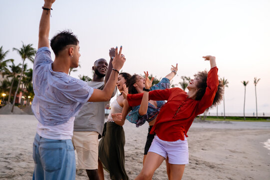Happy young people embracing the beach lifestyle, dancing barefoot in the sand, celebrating freedom