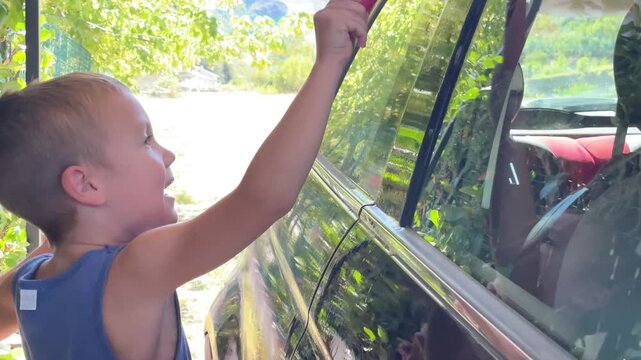 horizontal video of boy carefully helping to wash the car window. concept of involving children in family chores, fostering helpfulness, and encouraging quality family time spent productively