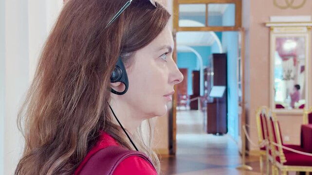 A woman listens attentively to an audio guide inside Catherine Palace in Pushkin, Saint Petersburg. The elegant museum hall inspires a calm, curious feeling of wonder.