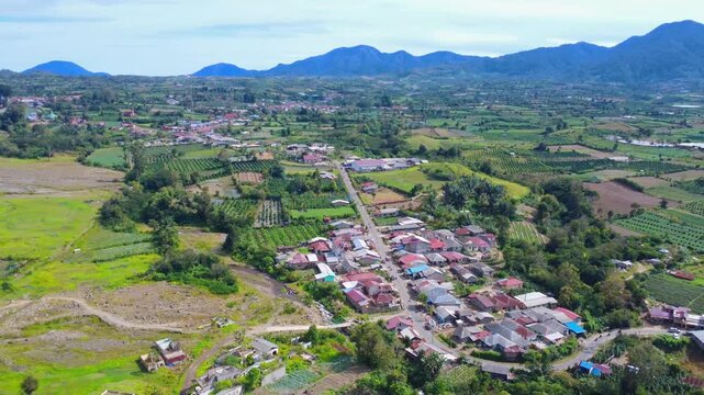 Aerial view of Mount Sinabung and rural village with lush green fields and agricultural land in Naman Teran, North Sumatra, Indonesia.