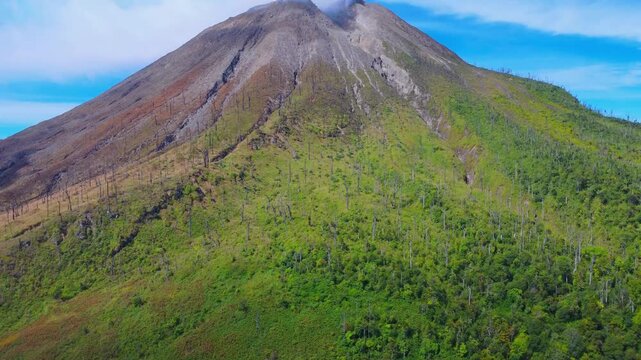 Aerial view of Mount Sinabung showing volcanic slopes with lush green vegetation and charred trees in Naman Teran, North Sumatra, Indonesia.