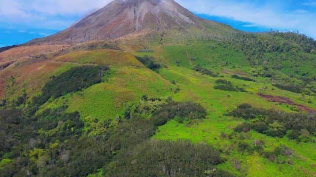 Aerial view of the volcanic peak of Mount Sinabung surrounded by lush green slopes and vegetation in Naman Teran, North Sumatra, Indonesia.