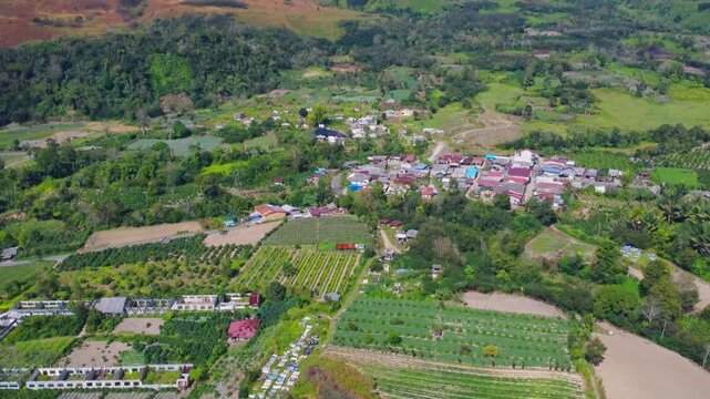 Aerial view of Mount Sinabung overlooking lush agricultural fields and a small village in Naman Teran, North Sumatra, Indonesia.