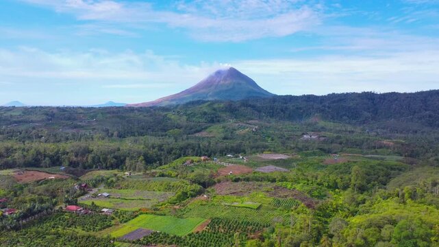 Aerial view of Mount Sinabung volcano with lush green agricultural fields and forests in Naman Teran, North Sumatra, Indonesia.