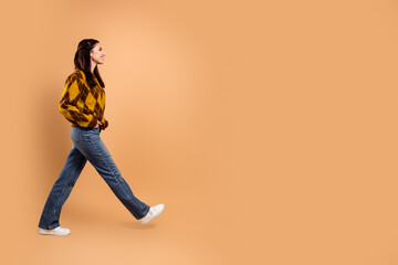 Young woman walking confidently in a yellow patterned sweater and jeans on an orange background,...