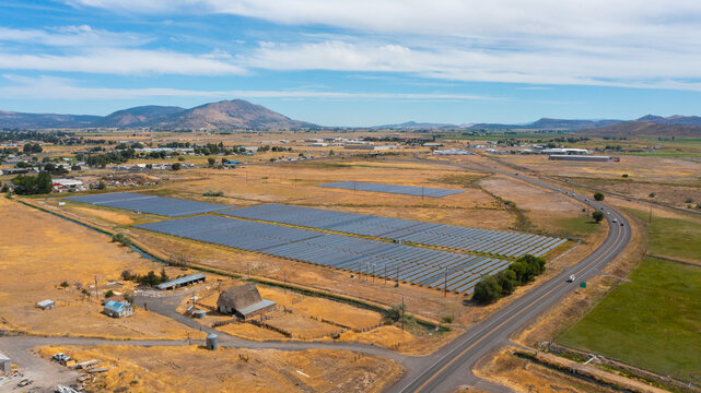 Aerial view of a solar farm with rows of photovoltaic panels situated in a dry rural landscape near a road and farm buildings in Klamath Falls, Oregon, United States.