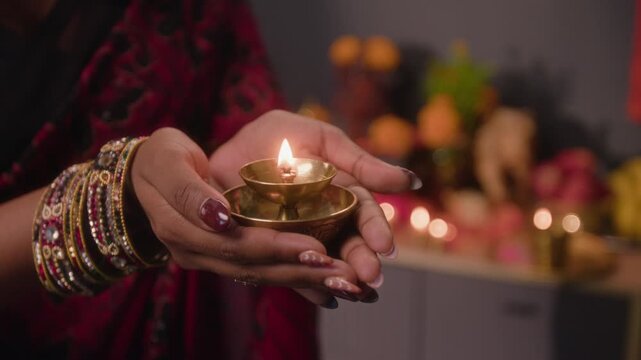 Close-up shot of unknown Indian woman holding lit brass diya oil lamp during traditional festival prayer ritual. Video suits Diwali holiday campaigns, cultural advertising, and religious projects