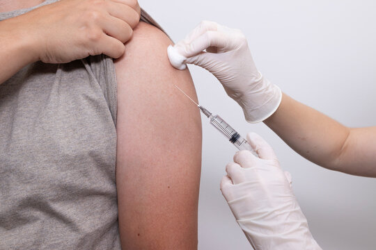 Doctor preparing vaccine injection near patient's upper arm while holding syringe and cotton pad. Concept of flu vaccination, measles vaccination, mumps vaccination, hepatitis B vaccination.