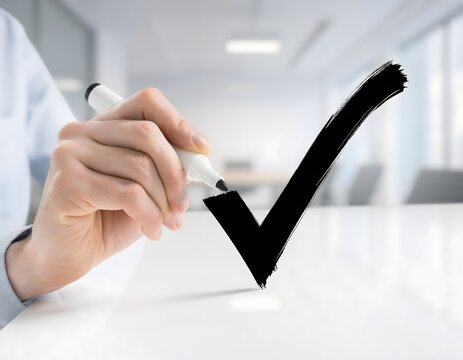 Hand holding marker pen drawing big bold black checkmark tick on transparent glass board in bright office.