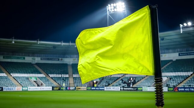 Bright yellow soccer corner flag on a green pitch in an illuminated stadium at night