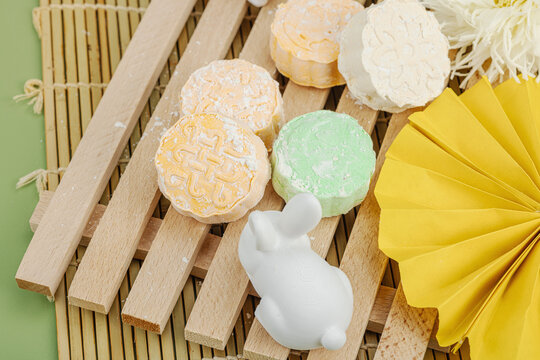 Traditional mooncakes on a wooden stand with ceramic rabbits, paper fan, chrysanthemum, bamboo mat