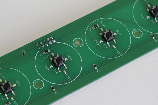 Macro shot of a green printed circuit board PCB with surface mount push buttons SMD components and electronic circuitry trace lines