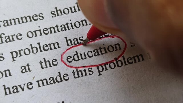 Student fingers holding red ink pen marking and highlighting Education word or text printed on news article or magazine. Abroad or overseas education scam or fraud crisis concept.