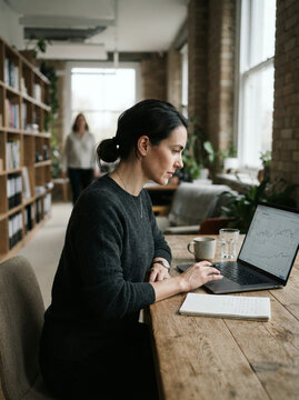 Woman typing on a laptop at a wooden table in a brick-walled office study