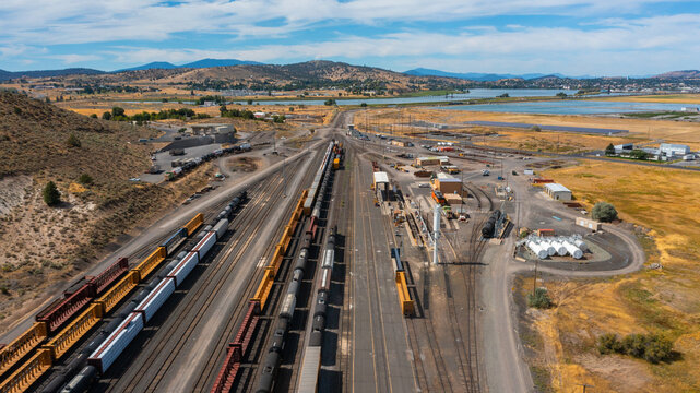 Aerial view of a busy rail yard with numerous freight cars parked on parallel tracks, industrial facilities, and dry landscape in Klamath Falls, Oregon, United States.