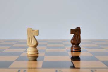 Light and dark chess knights face each other on a glossy wooden board. The minimal duel represents competition, confrontation, and strategic opposition © Hanna