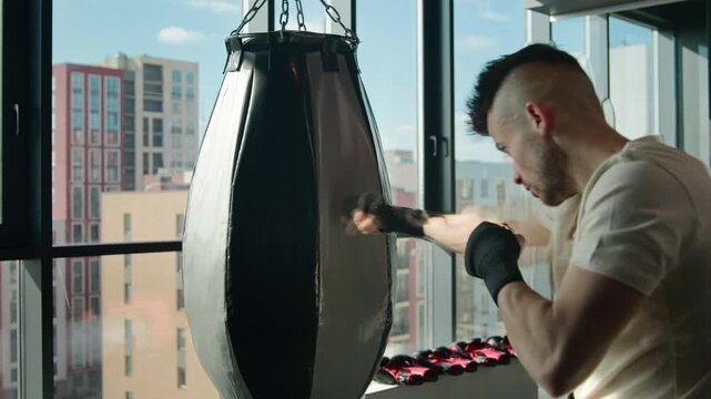 Caucasian boxer man training with punching bag in fitness gym strong fighter boxing athletic sportsman wearing gloves box powerful punches exercises muscular guy workout strength equipment sport club