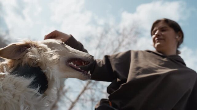 Woman interacts with white dog outdoors holding food as excited canine eagerly reaches up. scene features bright daylight and natural surroundings capturing moments of connection