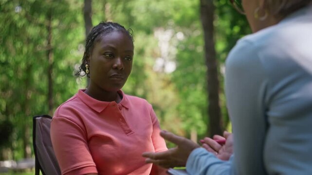 Young African American woman listening to counselor during outdoor psychotherapy session. Over shoulder shot fits mental health campaigns and medical projects