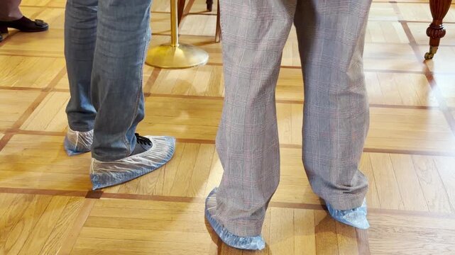 Visitors wearing shoe covers stand on a polished parquet floor inside the historic Lyceum in Pushkin, Saint Petersburg. The scene inspires a quiet feeling of respectful care.