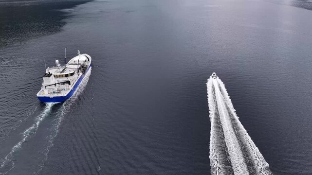 Aerial view of a wellboat and a smaller motorboat creating wakes as they navigate the calm waters of a fjord in Liabygda, More og Romsdal, Norway.