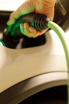 Hand connecting green charging cable to electric car, symbolizing eco-friendly transportation.