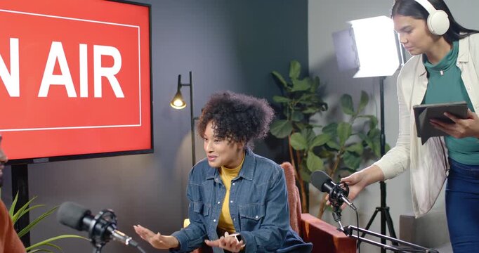 African American woman in denim speaking with ON AIR sign glowing, crew moving mic for recording