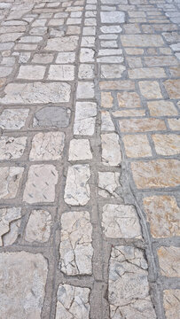 An angled overhead view shows the textured surface of an ancient stone pavement on a street in Baska on Krk Island in Croatia.