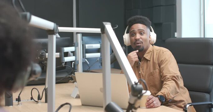 Co-hosts' African American host holding cup listening and reacting to cohost comment during podcast