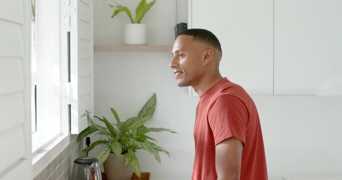 African American man leaning at counter peering via shutters at sun eyeing kettle smiling