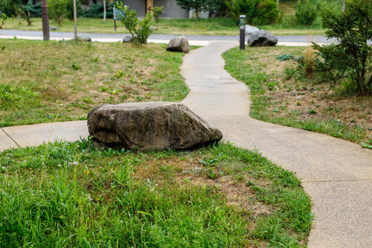 Serene winding concrete path through a green park with large rocks and lush grass.