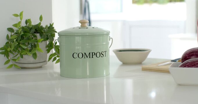 Camera is pushing forward, showing pastel green compost bin on glossy counter for kitchen display