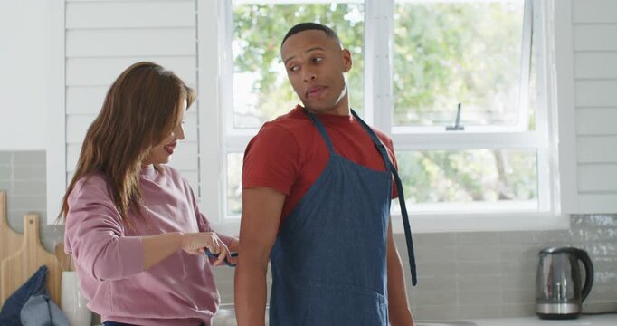 African American couple adjusting denim apron straps with loose strap in kitchen, preparing dinner