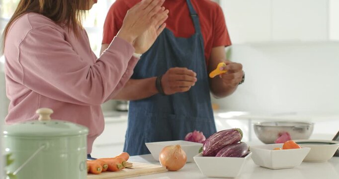 Couple African-American man and Asian woman reaching yellow peeler peeling carrots kitchen laughing