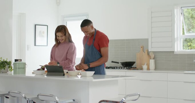 African American couple at kitchen island man in apron prepping while woman following tablet recipe