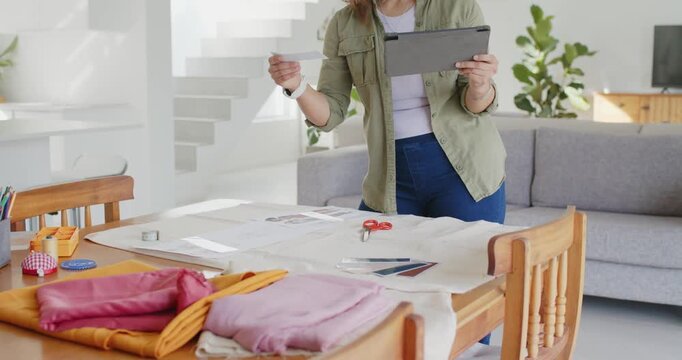 Asian woman using tablet selecting swatch and arranging layout for sewing on dining table at home