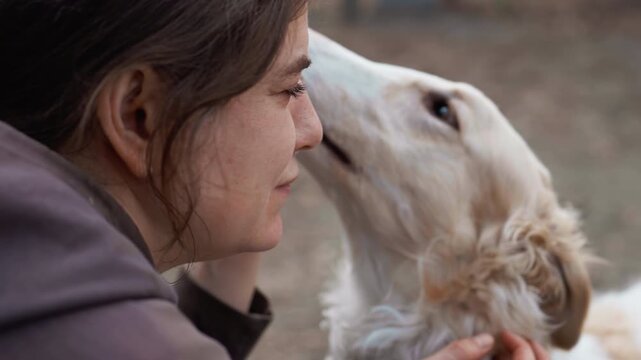 Woman interacts closely with white dog gently petting and feeding it in outdoor setting. focus remains on intimate connection between them emphasizing their bond without significant camera