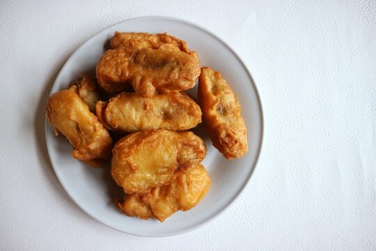Traditional fried banana with a golden, crispy looking batter coating, served on a white plate.