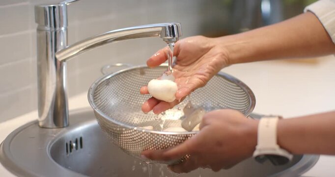 Hands rinsing button mushrooms in metal colander under running faucet for cooking, draining water