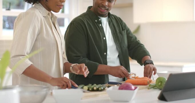 African American couple using peeler on carrots, slicing zucchini in kitchen following tablet