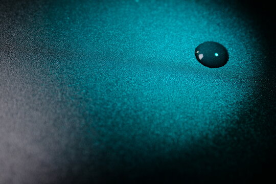 Cyan water droplet on dark textured surface with copy space