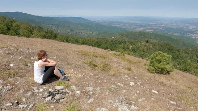Fit senior woman in top shape and excellent physical condition sitting on a mountain top, resting and enjoying the scenic view. Concept of active aging, wellness and relaxation in nature.