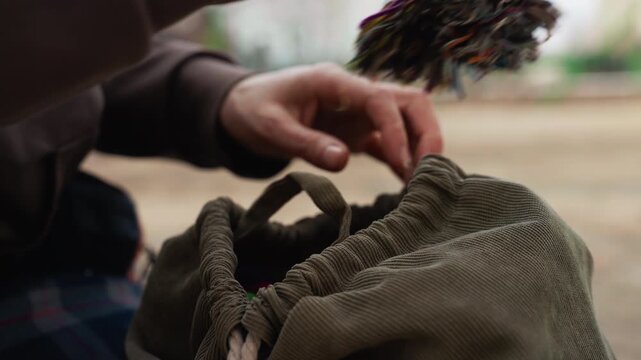 Person hands manipulate drawstring on olive green fabric bag revealing colorful objects inside. focus remains tightly on hand movements and texture of corduroy material throughout sequence