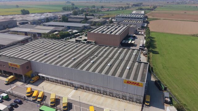 San Giuliano Milanese, Italy - 05 September 2026: Aerial view of the DHL Express facility with large warehouses, loading docks, and yellow delivery trucks in an industrial area.