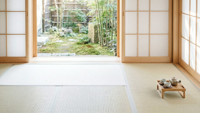涼しい自然光が差す広い畳の和室で竹と苔の坪庭を望み右下に木製茶台と茶器を置いた障子の室内