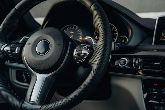 Close-up view of a modern car steering wheel with control buttons and dashboard instruments visible, showcasing a sleek interior design and high-quality materials