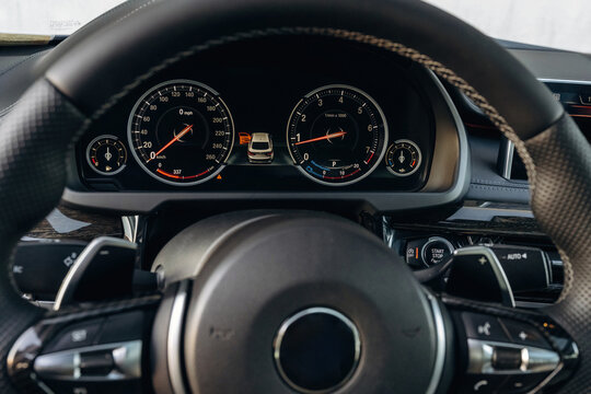 Close-up view of a modern car dashboard featuring speedometer and tachometer gauges, steering wheel with controls, and a sleek interior design