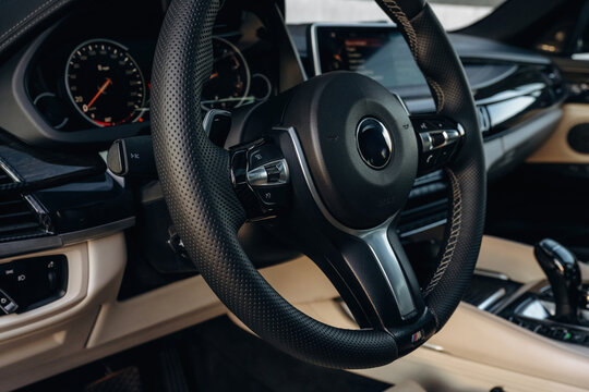Close-up view of a modern car steering wheel with leather grip and control buttons, showcasing the dashboard and interior design elements in a luxury vehicle