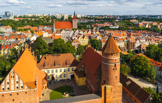 Aerial view of the historic Castle of Warmian Chapter with its iconic tower and red brick architecture surrounded by old town rooftops in Olsztyn, Warmian-Masurian Voivodeship, Poland.