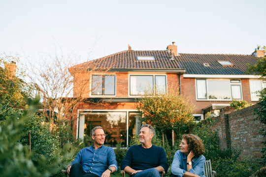 Three Friends Relaxing in Backyard Garden at Dusk in Front of Suburban House